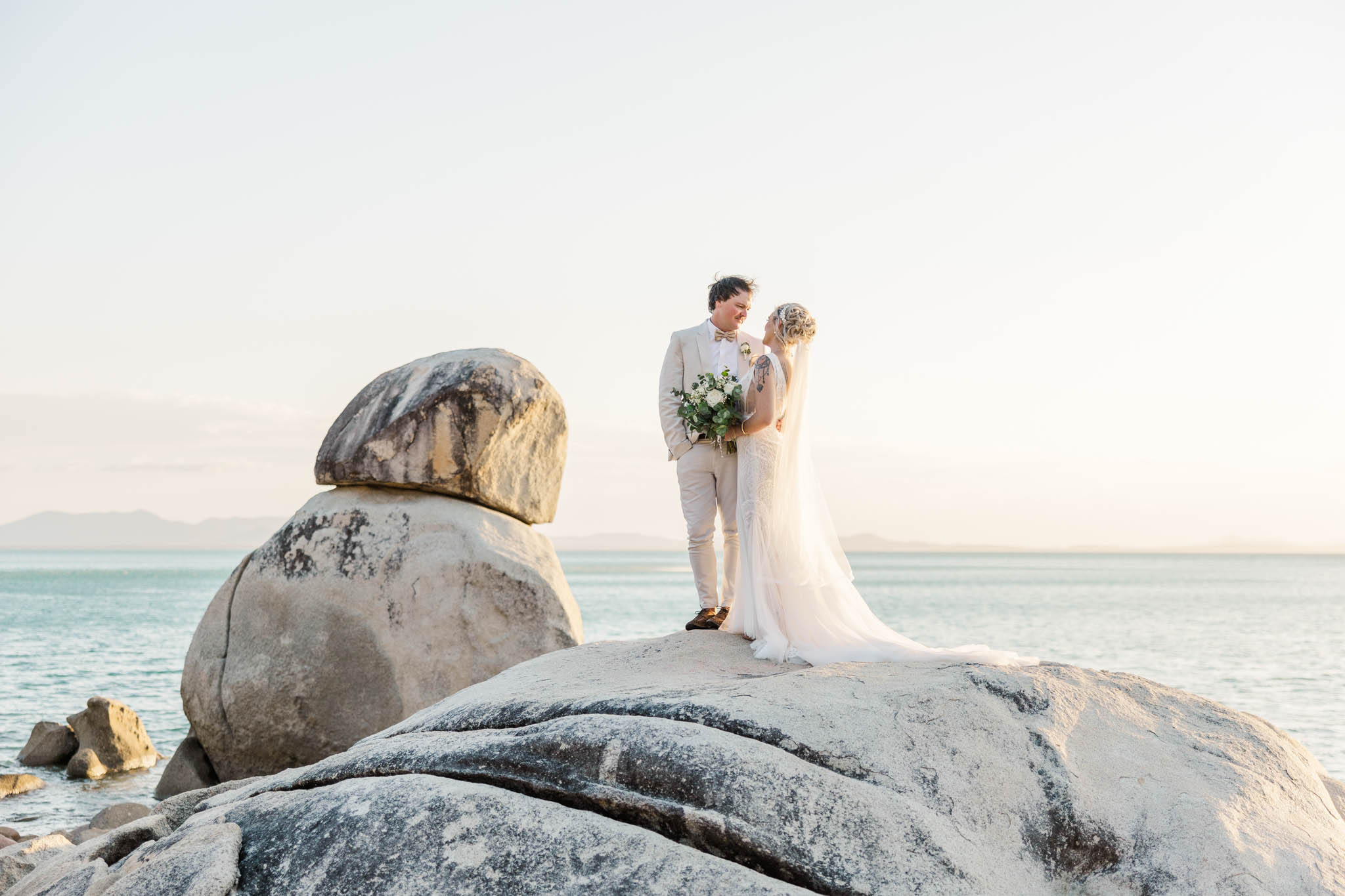 Bride and groom standing on large boulders in front of whitsunday waters during sunset portraits.