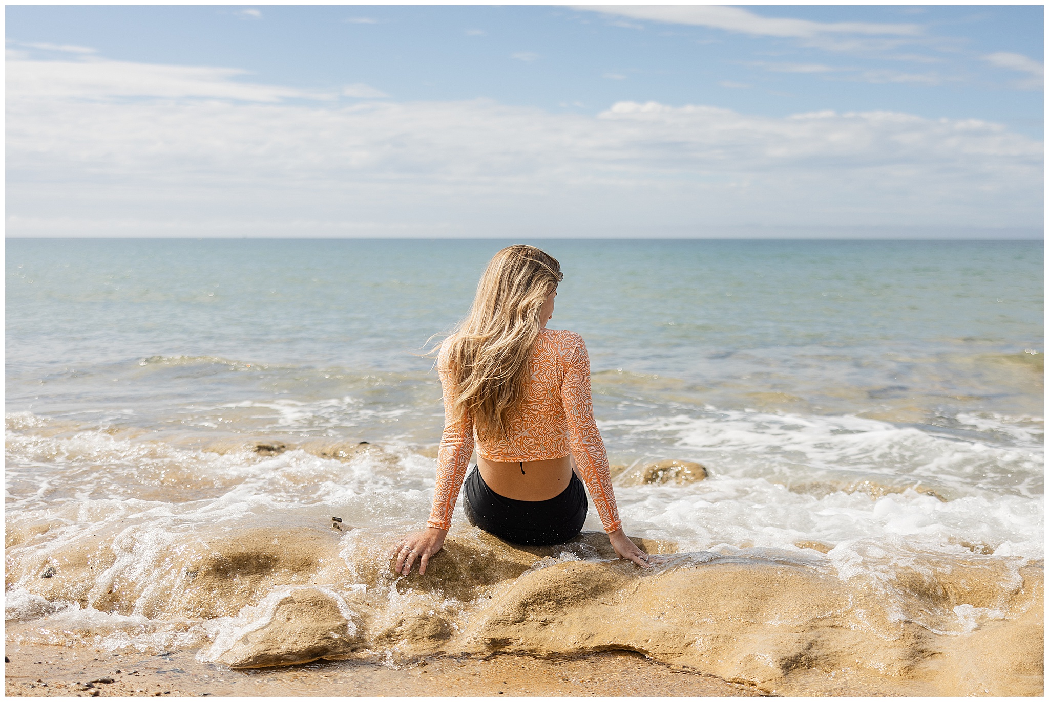 Model sitting on rocky beach wearing swimwear brand Bussin Style Co