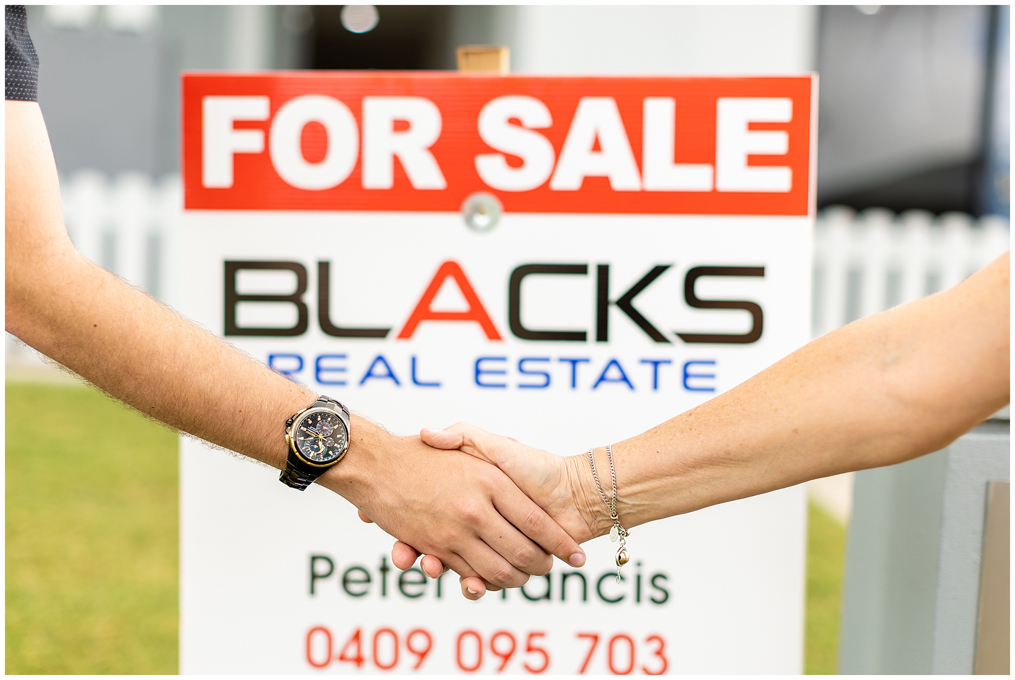 Close-up of a real estate agent’s handshake with a client in front of a ‘For Sale’ sign, symbolising trust and success in Mackay real estate.